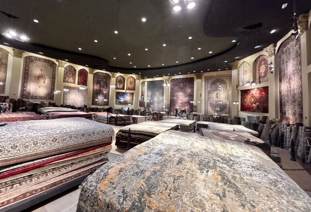 Rug Gallery, large rugs hang on the walls and piles of different size rugs fill the center of this large room, an old movie theatre, refurbished into modern day gallery.